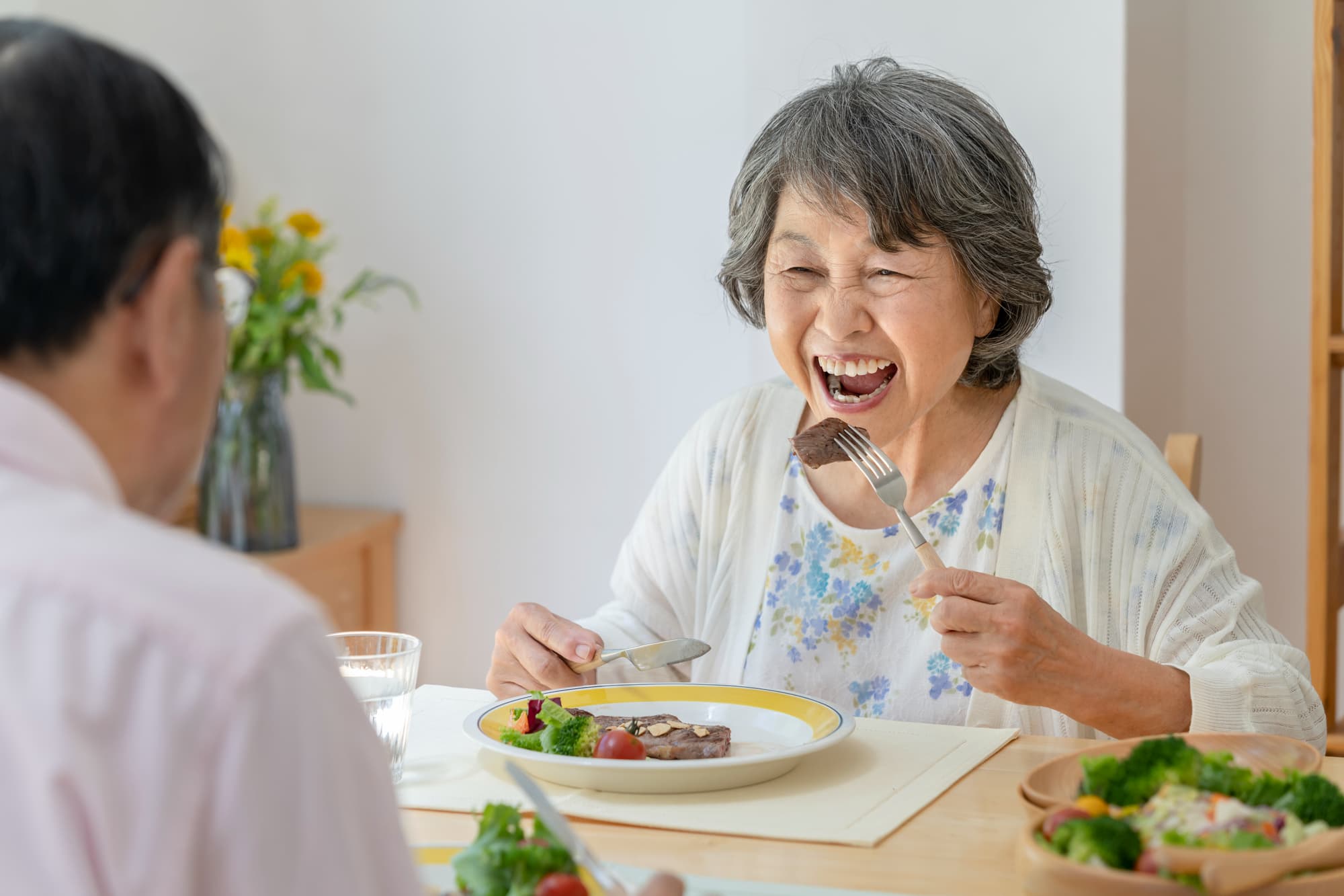 入れ歯でステーキを食べる笑顔の女性